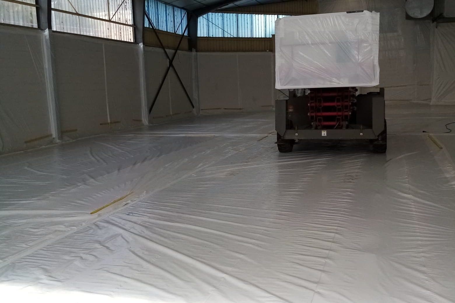 Zone confinée sous bâche blanche, nacelle élévatrice protégée par un film