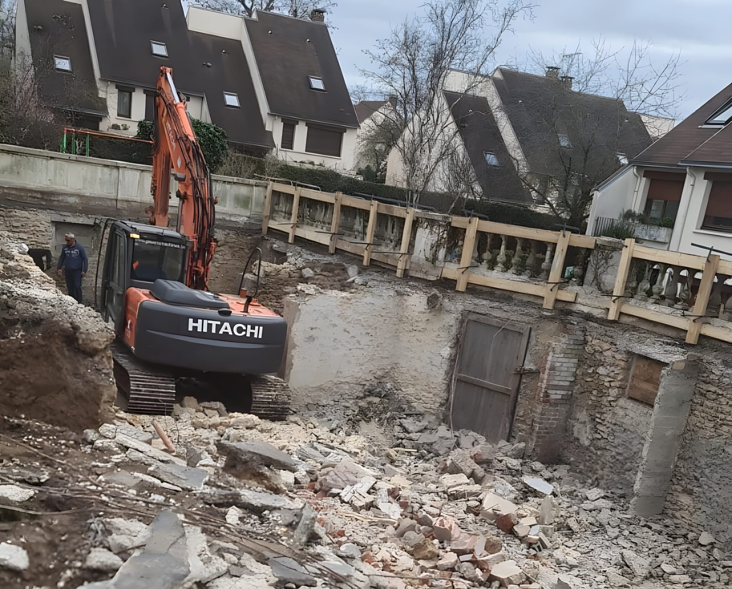 Pelle Hitachi dans une cour en démolition, entre murs en pierre et gravats